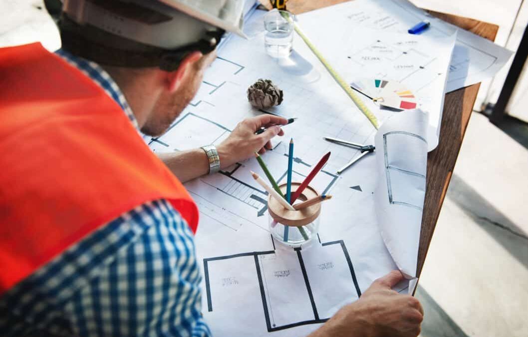 Mechanical engineer wearing a hard hat leaning on a table while checking a white sketch plan