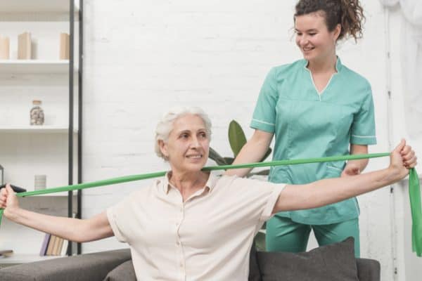 physical therapist assisting old woman stretching with green exercise band
