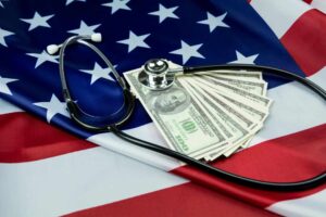 Health insurance illustrated by american flag in the background, with stethescope and stack of hundred dollar bills